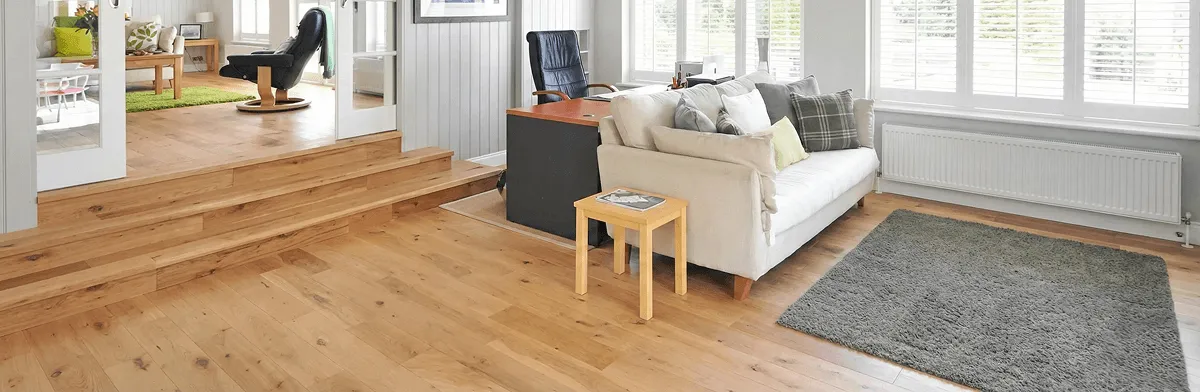 A modern living room with professionally installed laminate flooring, a beige sofa, a small side table, a gray rug, and large windows with white shutters in Overland Park, KS